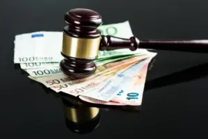 Der Hammer eines Richters liegt auf einem Stapel Euro-Banknoten im Wert von 20, 50 und 100 Euro. Vor dem Hintergrund einer glänzend schwarzen Oberfläche symbolisiert diese Szene die Schnittstelle zwischen dem Pflichtteilsanspruch im Erbrecht und allgemeineren juristischen und finanziellen Themen.